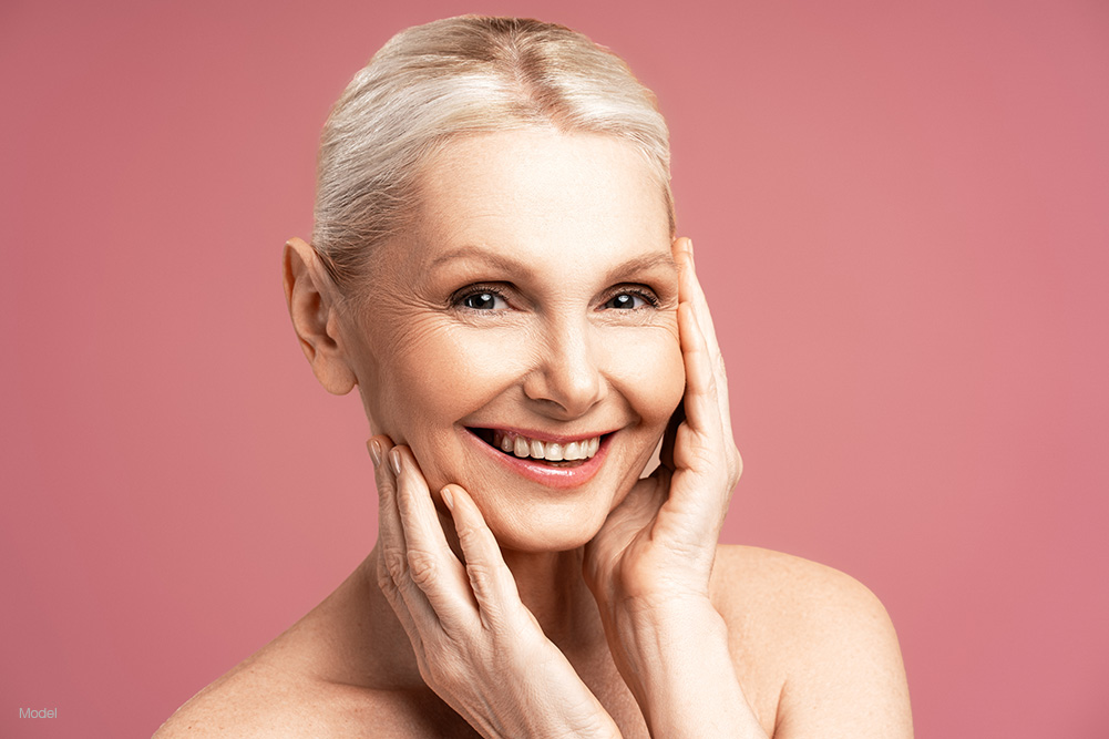 Mature woman touching her face against a pink background